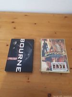 Photo of both DVD box sets, Bourne Trilogy on left and Indiana Jones 4 Film Set on right, placed on wooden table.