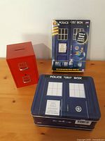 Doctor Who TARDIS lunchbox with front design and red mini filing cabinet side-by-side on wooden surface