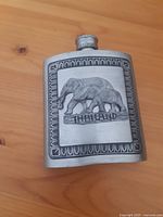 Front view of a rectangular metal flask with an embossed elephant design and "THAILAND" text on the front.