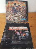 Photo showing front album covers of 'Captain Fantastic and the Brown Dirt Cowboy' and 'Don't Shoot Me I'm Only the Piano Player' albums by Elton John.