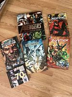 Five comic books placed on a wooden floor, titles visible including Avengers, Nightwing, Justice, Brooklyn Animal Vol. 1, and Ab Irato.