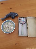 Full set showing the jade handled mirror in its original box, the stone dolphin figurine, and the round porcelain plate arranged on a wooden surface.