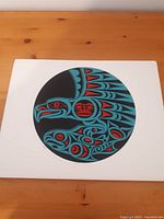 Front view of the art print showing the stylized First Nations bird design in blue, red, and black within a circular black background on white mat board.