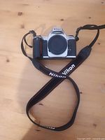 Front view of Nikon DSLR camera body with lens mount covered and Nikon branded strap attached.