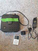 Photo showing Blackweb Bluetooth alarm clock with remote controller taped on top, power adapter, white Apple iPod Classic, and Nokia mobile phone with cord and headphones