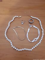 Photo showing full set of pearl necklace, two bracelets, and two rings laid out on wooden surface