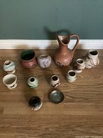 Photo showing eleven Southwestern Native American style pottery items including vases, jug, and small pots with varying designs and colors arranged on a wooden floor.