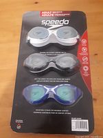 Front view of Speedo 3-pack adult swim goggles in original sealed card packaging on wood surface.