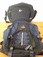 Two bags shown together: a black carry-on luggage bag and a dark blue/black PlayStation backpack