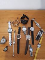 Overview photo showing all 12 watches arranged on wooden table, including wristwatches with varied straps and two pocket watches.