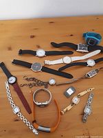 Lot overview showing all watches including a blue digital watch, various leather strap wristwatches, and metal bracelet watches.