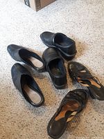 Three pairs of women's shoes on carpet: two black slip-ons and one pair of brown strappy sandals.