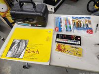 Yellow Strathmore sketchbook, colored pencils, oil pastels, paintbrushes on table with the organizer closed nearby