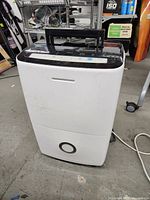 Front view of black and white Frigidaire dehumidifier on floor showing portable design and water collection area at bottom.