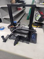 Full view of the Creality 3D printer sitting on a table in an industrial environment, showing the metal frame, extruder, print bed, and control panel.
