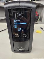 Front view of CyberPower 1000VA AVR UPS with digital display showing power on and voltage readout 121V.