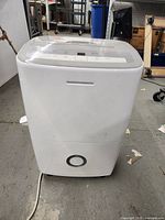 Front view of white Frigidaire dehumidifier on concrete floor with visible power cord