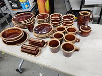 Full view of the entire Hull ovenproof stoneware set arranged on a white table showing a variety of cups, plates, bowls, butter dishes, sugar bowl, and a pitcher.