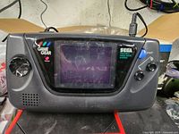 Front of Sega Game Gear console powered on, showing screen and control buttons.