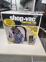 Front view of the Shop-Vac Contractor box showing product image, key features including 5 gallon capacity and 5.5 HP peak motor, and mention of included accessories and filter bag.