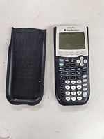 Front view of TI-84 Plus graphing calculator and black protective cover on white surface.