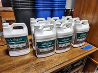 Overview of ten 1-gallon white plastic containers of Valspar Protective Sealer Wet Look with green and white labels on a wooden surface.