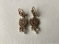 Two earrings face up on white background showing filigree front and dangling pearls