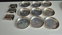 Overview of nine round silver coasters and three rectangular match holders on white background