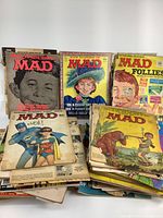 Stack of MAD magazines arranged on table, showing a variety of covers including Batman parody and Alfred E. Neuman issues