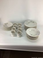 Front view of 36-piece dish set including dinner plates, salad plates, soup bowls, and coffee mugs with floral designs on white ceramic.