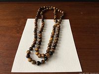 Full view of the long tiger eye bead necklace placed on white paper on wooden surface.