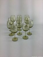 Photo of eleven vintage green etched wine glasses arranged in rows showing front and side views, highlighting etched designs and condition.
