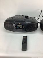 Black JVC boom box with cassette deck, digital AM/FM tuner, and remote control in front, powered on.