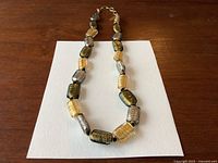Full view of the Murano glass bead necklace showing the alternating black, gold, and silver foil-lined beads separated by small black spacers.