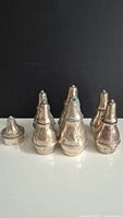 Seven tarnished sterling silver shakers arranged in group on white surface against black background