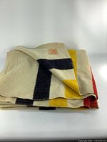 Folded beige wool blanket with black, yellow, and red stripes