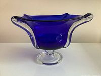 Side view of the hand-formed cobalt blue glass pedestal bowl showing the clear glass rim and foot on white background.