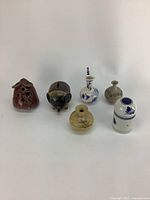 Six vintage small pottery and ceramic decorative items arranged in a row on a white surface, showing details and minor wear.