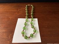 Full view of green Murano glass bead necklace laid on a white background showing bead sizes and arrangement.