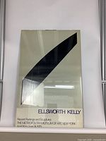 Full view of unframed poster leaning against white background, showing black curved shape and text