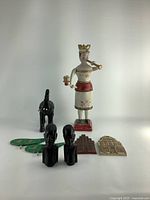 Front view showing all eight items: large painted female figurine, black horse, two black busts, two green bird decorations, two architectural plaques.