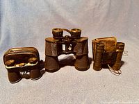 Three pairs of vintage binoculars, including a large one with strap and two smaller ones with cases.