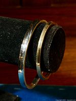 Two antique bangles on a black jewelry display stand, one sterling silver and one gold-filled hinged bangle.