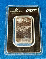Front view of silver bar in black and clear plastic packaging showing The Royal Mint logo, 007 logo, and silver bar details.