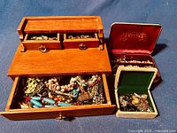 Wooden jewelry box with two small upper drawers and one larger lower drawer containing assorted jewelry pieces, next to two velvet-lined boxes with more jewelry inside.
