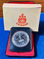 Overall view of 1978 Canadian silver proof dollar coin in plastic casing inside presentation case with official Canada booklet behind.