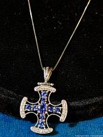 Close-up image of the Maltese cross pendant showing violet-blue and clear CZ stones set in a rhodium plated sterling silver cross with chain.