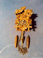 Full view of the carved wood cuckoo clock showing two pinecone weights and chains.