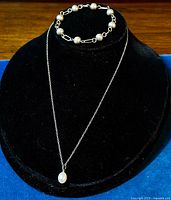 Front view of the necklace with faux pearl pendant and paperclip and ball silver bracelet displayed on black stand.