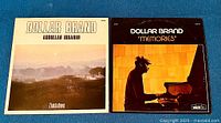 Both vinyl LP album covers side by side: 'Zimbabwe' on left, 'Memories' on right featuring piano playing profile photo.